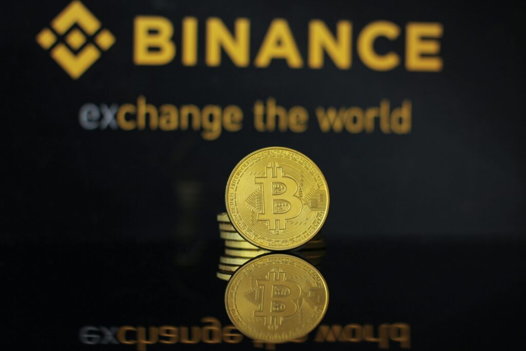 Close-up of a Bitcoin coin with Binance logo and text reflecting in dark surface.