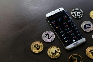 A collection of cryptocurrency coins and a smartphone displaying a digital trading platform.
