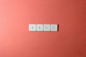 Close-up of keyboard tiles spelling 'sell' on a red background, minimalist design.
